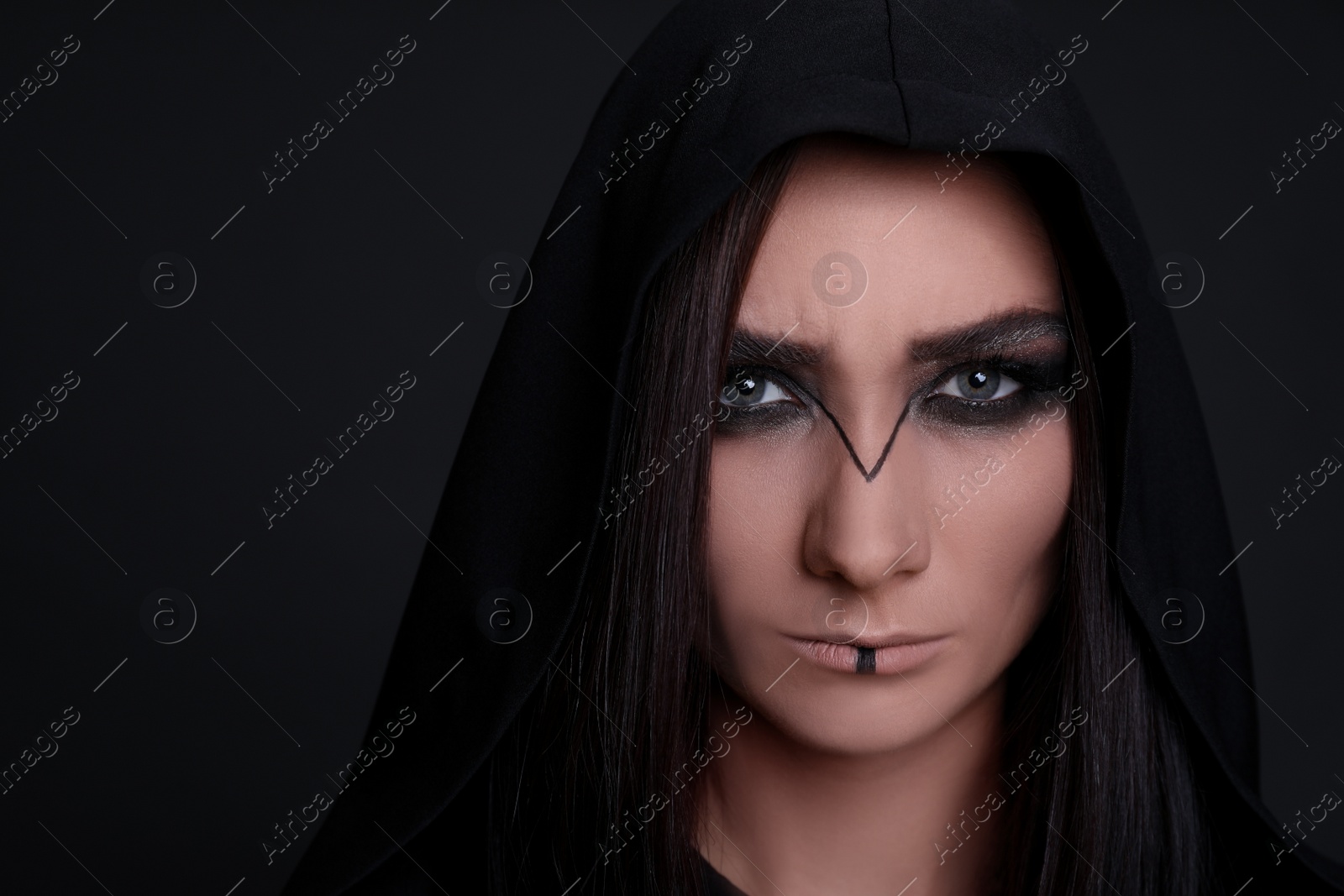 Photo of Mysterious witch in mantle with hood on black background, closeup. Space for text