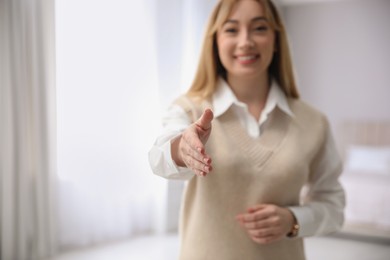 Photo of Happy young woman offering handshake indoors. Space for text