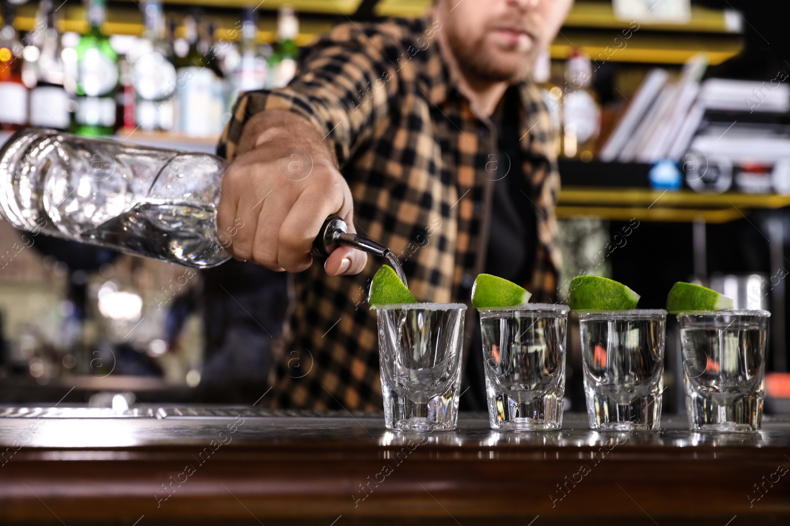 Photo of Bartender pouring Mexican Tequila into shot glasses at bar counter, closeup