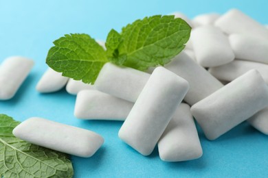 Photo of Pile of tasty white chewing gums and mint leaves on light blue background, closeup