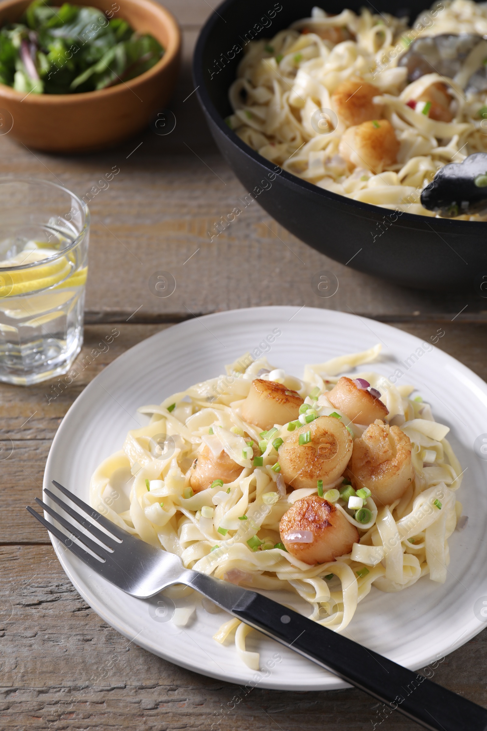 Photo of Delicious scallop pasta with onion served on wooden table