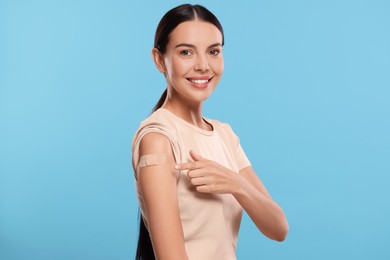 Photo of Woman pointing at sticking plaster after vaccination on her arm against light blue background