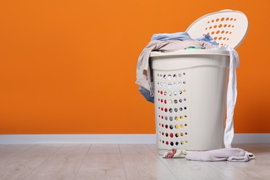 Photo of Laundry basket with clothes near orange wall. Space for text