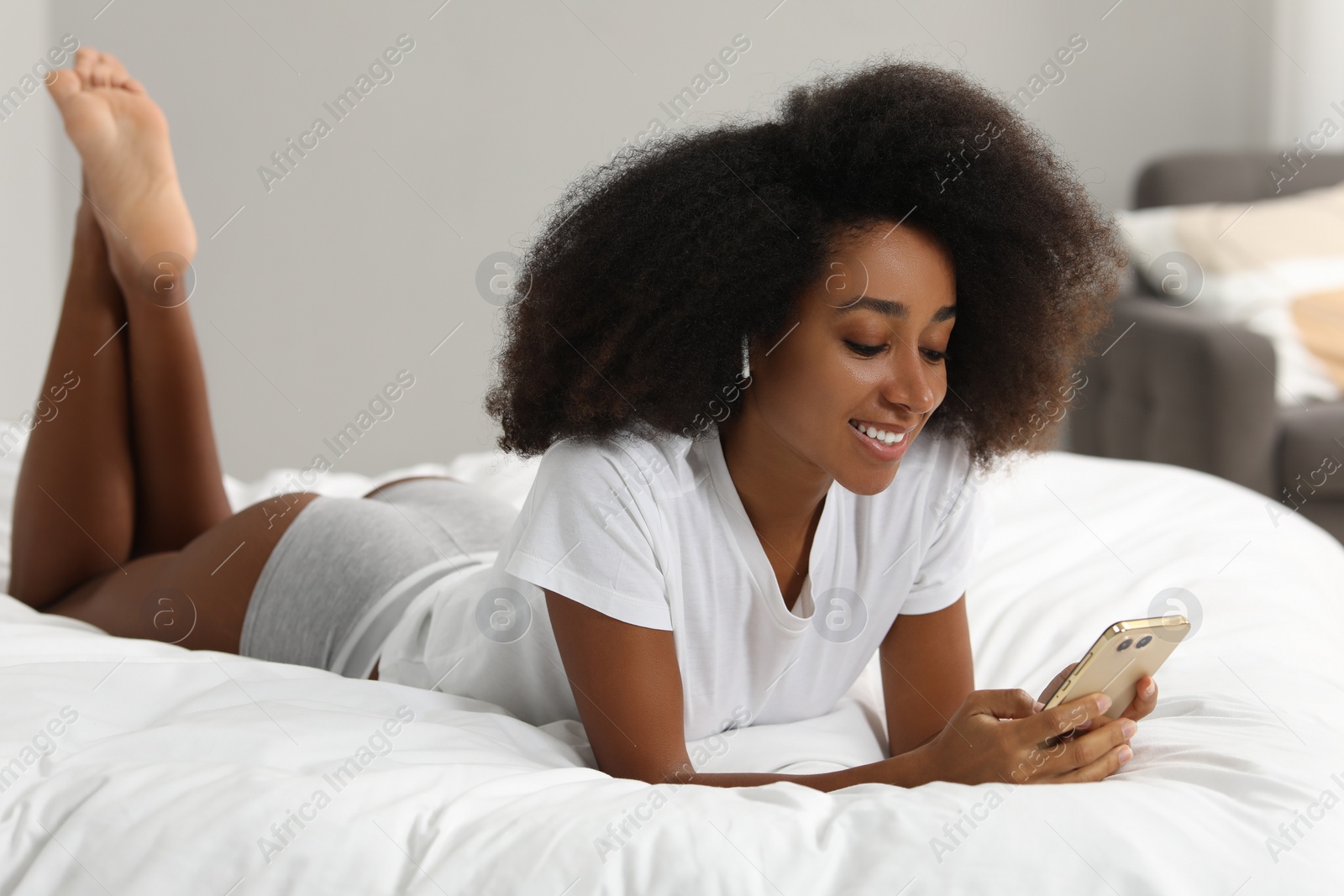 Photo of Beautiful woman in stylish underwear and t-shirt using smartphone on bed indoors