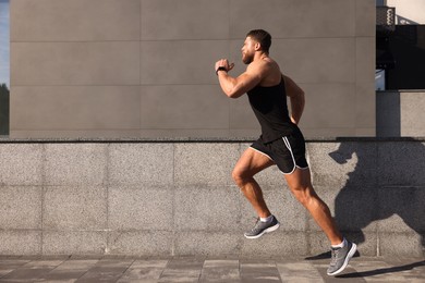 Young man running near building outdoors. Space for text