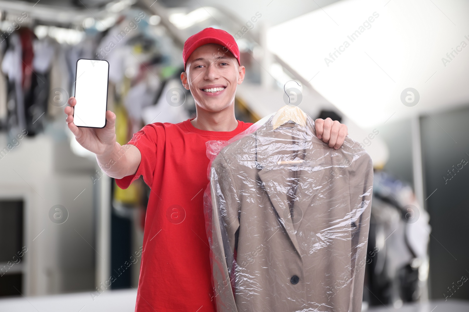 Image of Happy courier with jacket in plastic bag showing smartphone in dry-cleaning