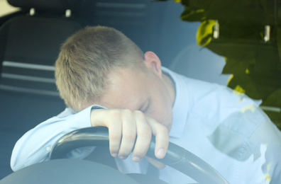 Tired young man sleeping on steering wheel in his car, view from outside