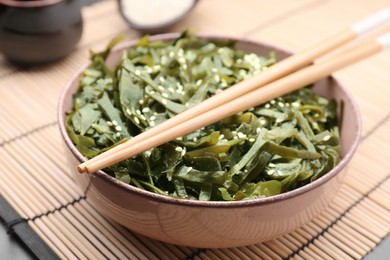 Photo of Fresh laminaria (kelp) seaweed in bowl and chopsticks on table, closeup