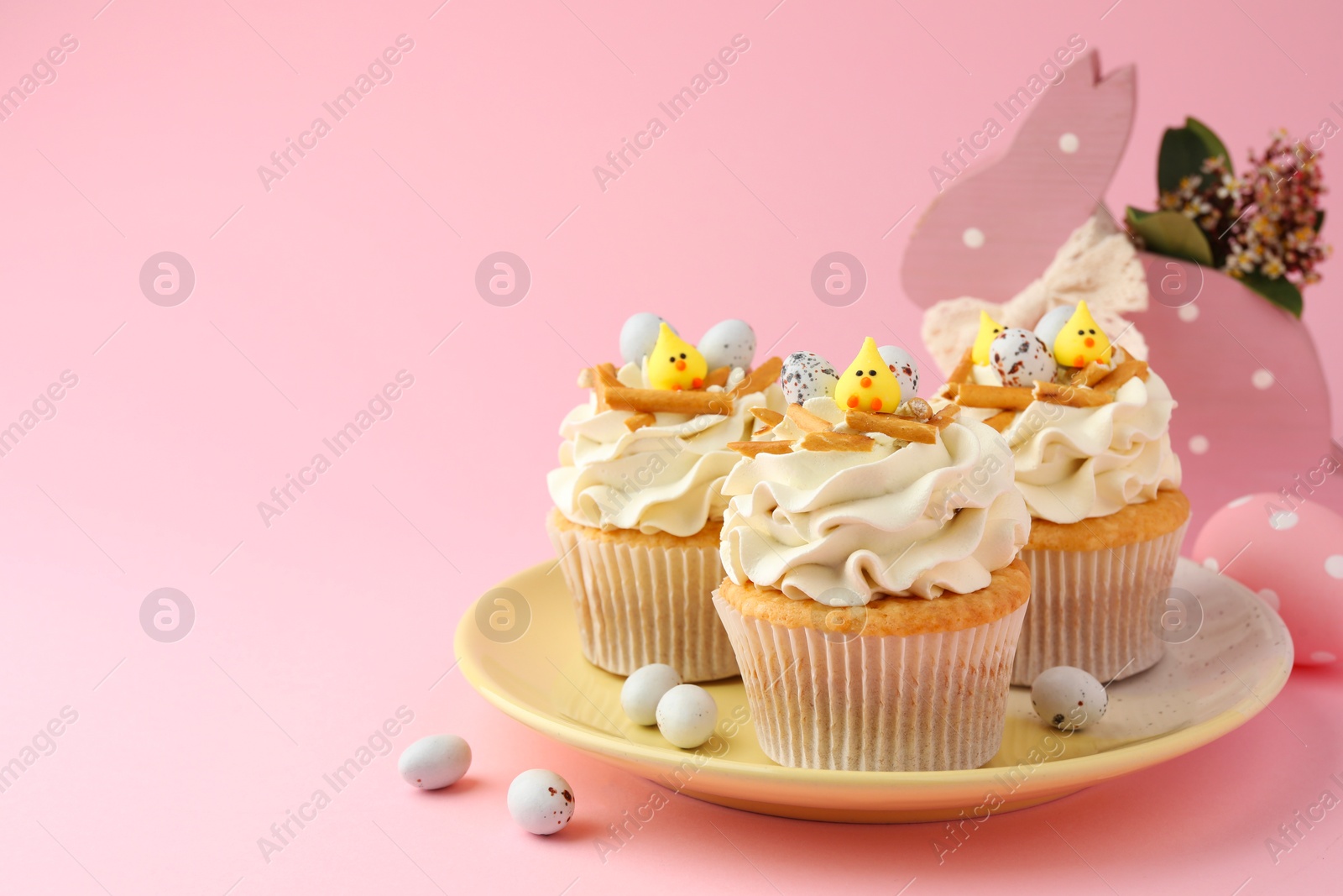 Photo of Tasty Easter cupcakes with vanilla cream and candies on pink background, space for text