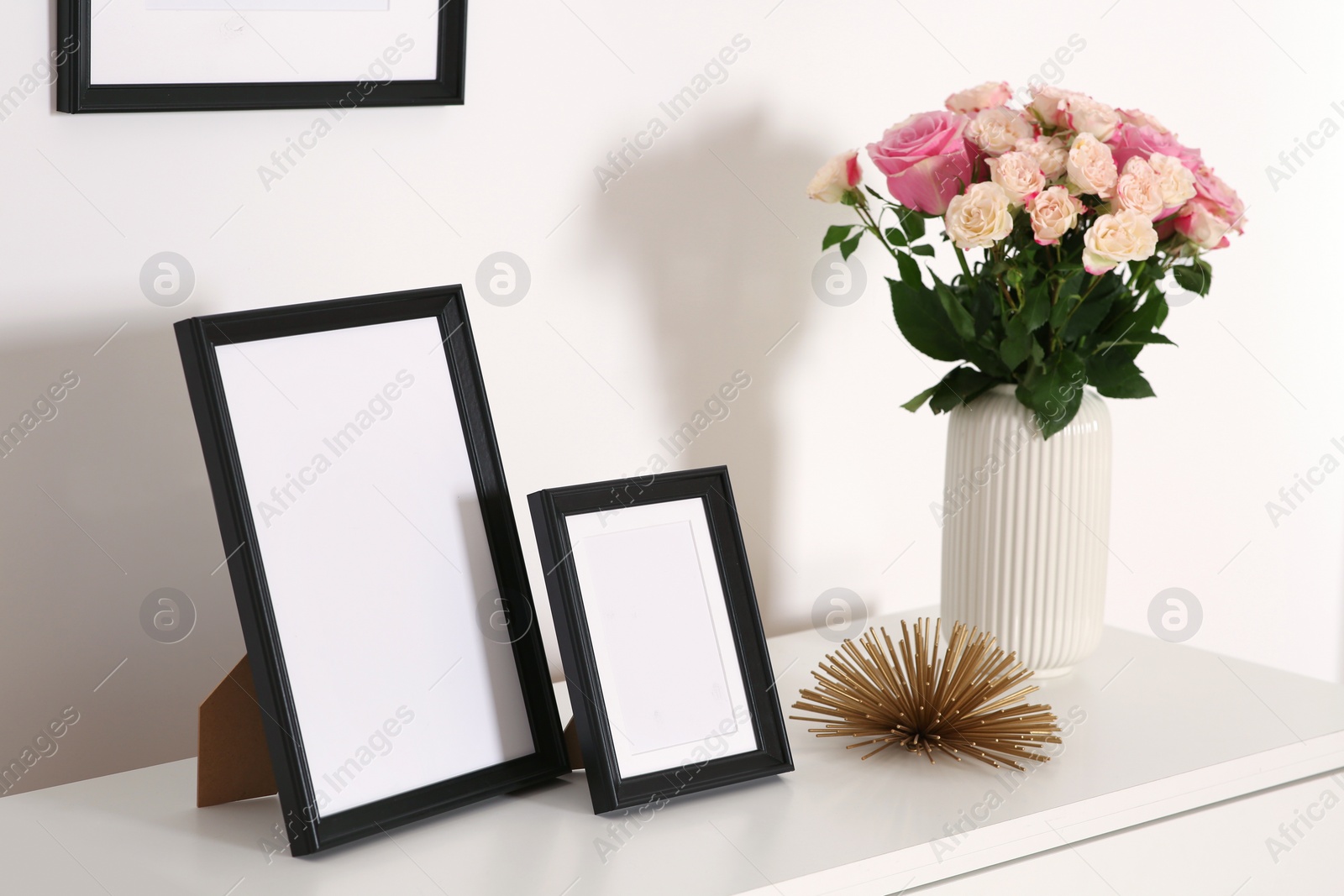 Photo of Empty frames and flowers on chest of drawers indoors