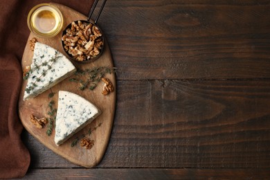 Tasty blue cheese with thyme, honey and walnuts on wooden table, top view. Space for text