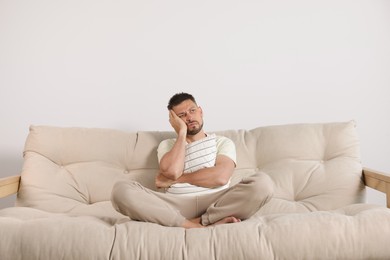 Photo of Sleepless man hugging pillow on sofa at home