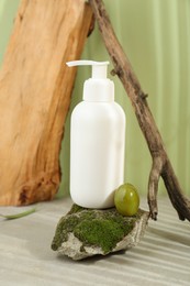 Photo of Bottle of cosmetic product with olive essential oil on stone with moss against light green background