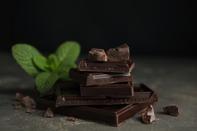 Photo of Tasty dark chocolate pieces with mint on grey table