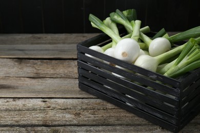 Black crate with green spring onions on wooden table, space for text