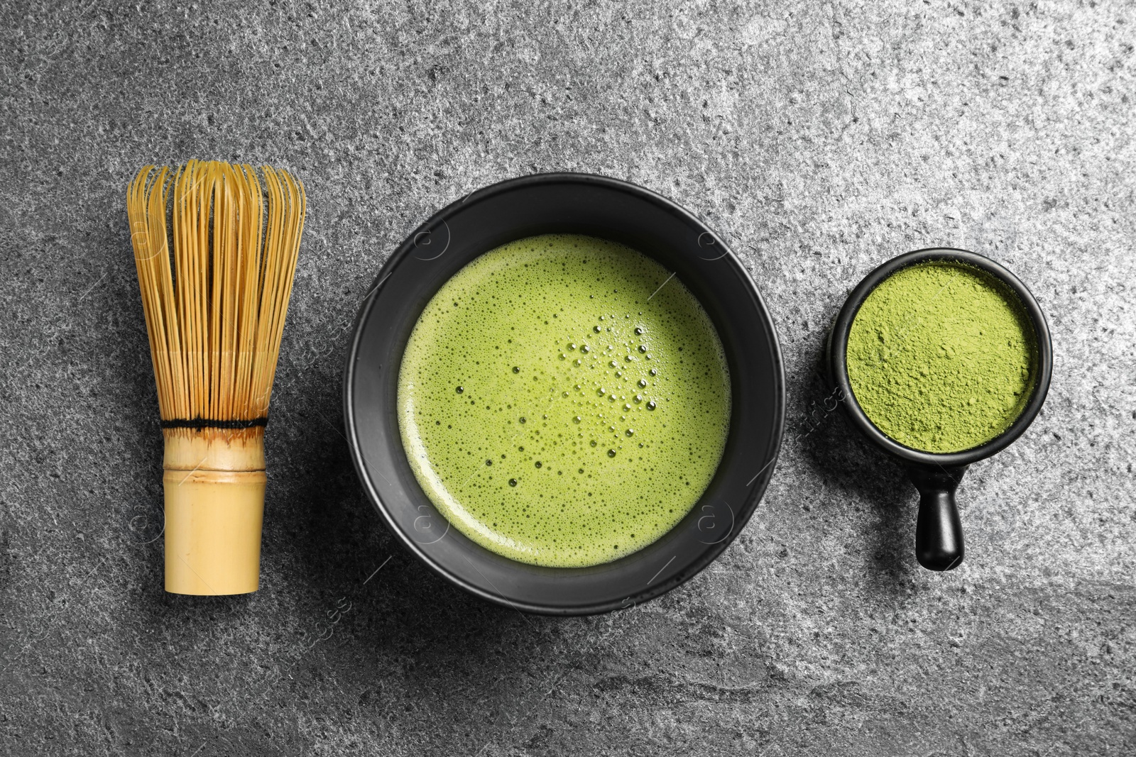 Photo of Cup of fresh matcha tea, bamboo whisk and green powder on grey table, flat lay