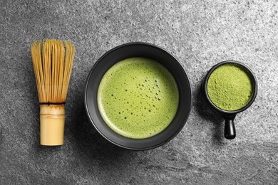 Photo of Cup of fresh matcha tea, bamboo whisk and green powder on grey table, flat lay