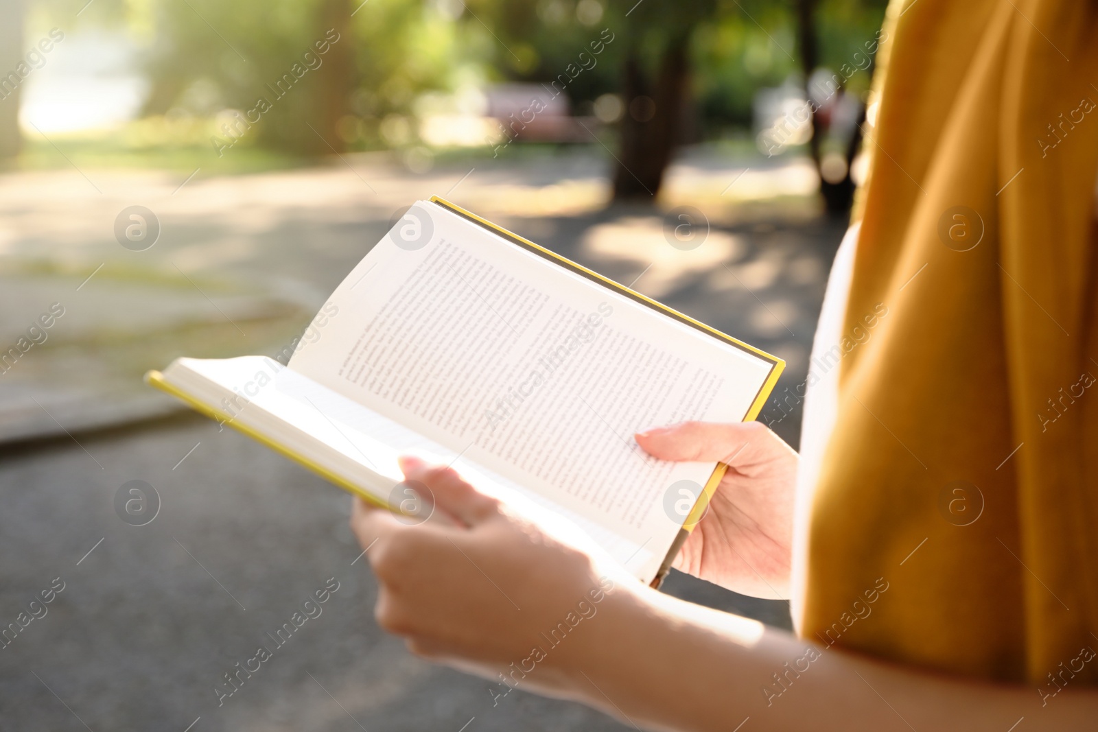 Photo of Young woman reading book outdoors, closeup view