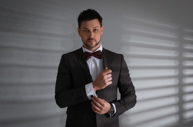 Man wearing stylish suit and cufflinks near white wall