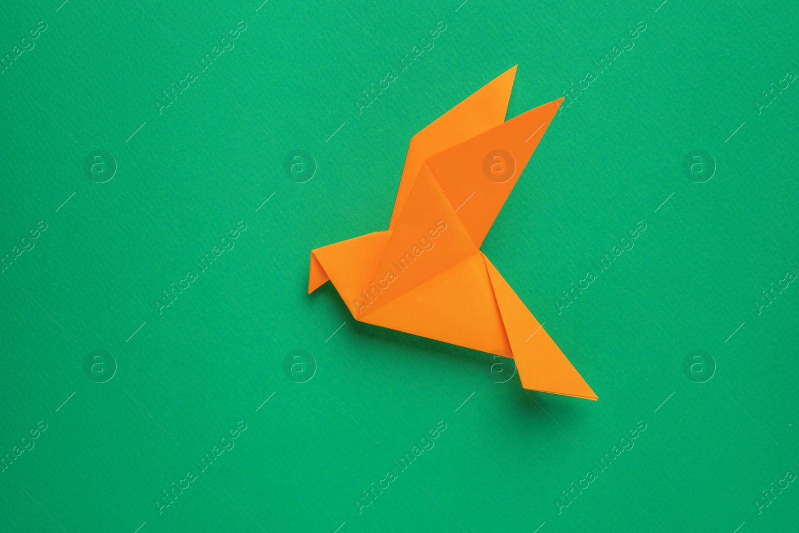 Photo of Beautiful orange origami bird on green background, top view