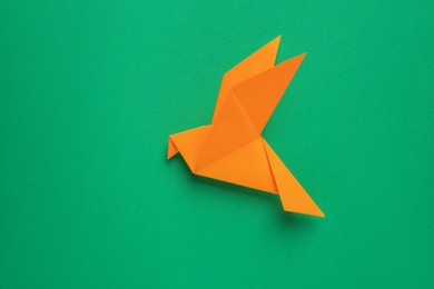 Beautiful orange origami bird on green background, top view