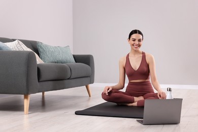 Woman in sportswear meditating near laptop at home, space for text