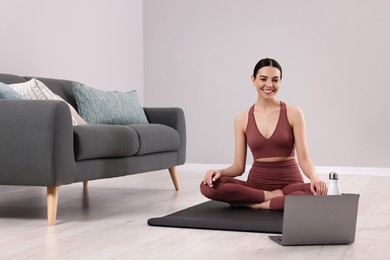 Photo of Woman in sportswear meditating near laptop at home, space for text