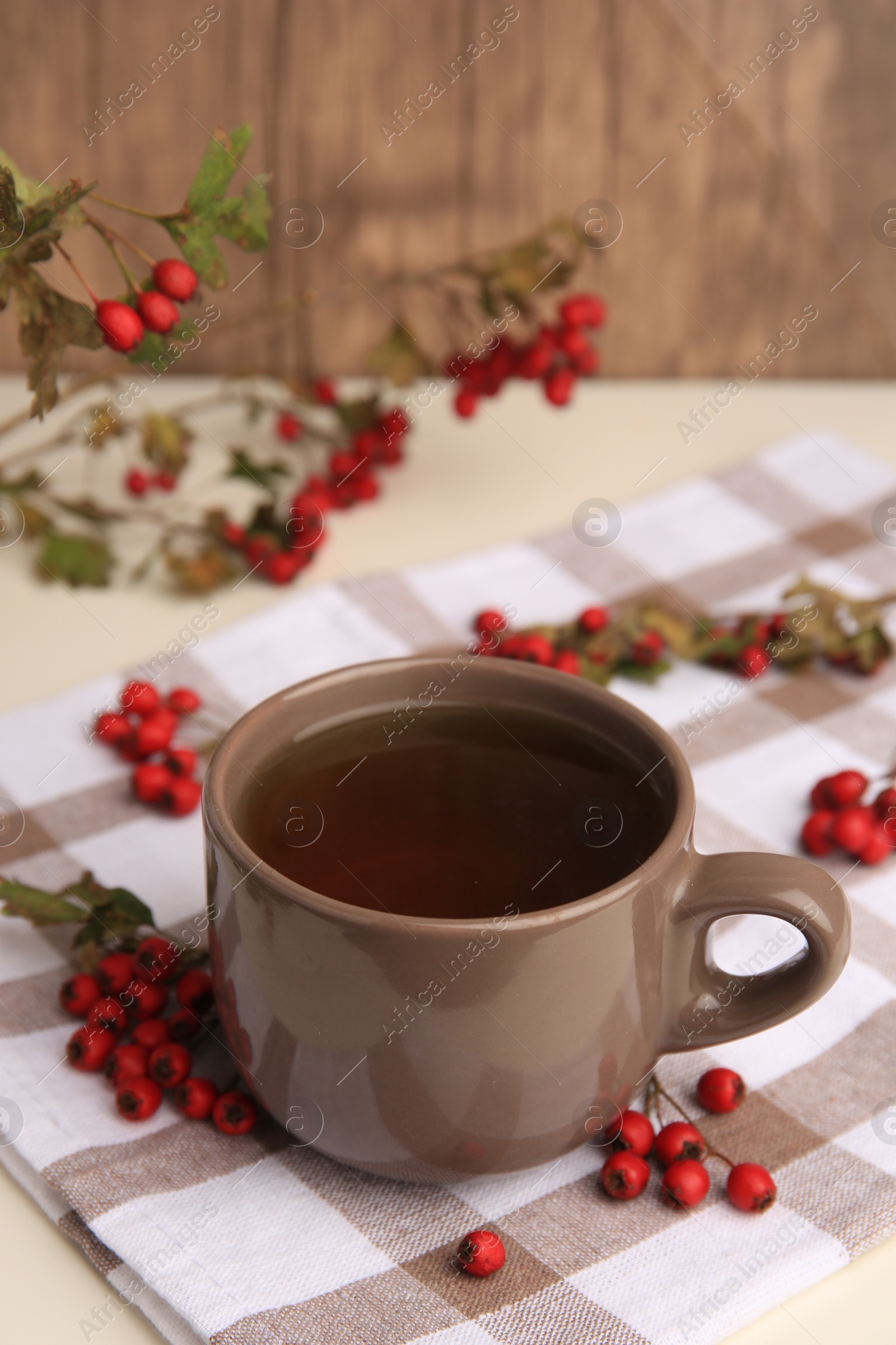 Photo of Brown cup with hawthorn tea and berries on beige table
