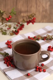 Brown cup with hawthorn tea and berries on beige table