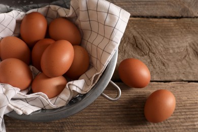 Chicken eggs in colander and napkin on wooden table