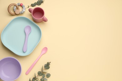 Photo of Set of plastic dishware and wooden toy on beige background, flat lay with space for text. Serving baby food