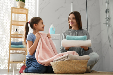 Mother and little daughter with clean laundry in bathroom
