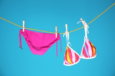 Beautiful bikini hanging on rope against color background