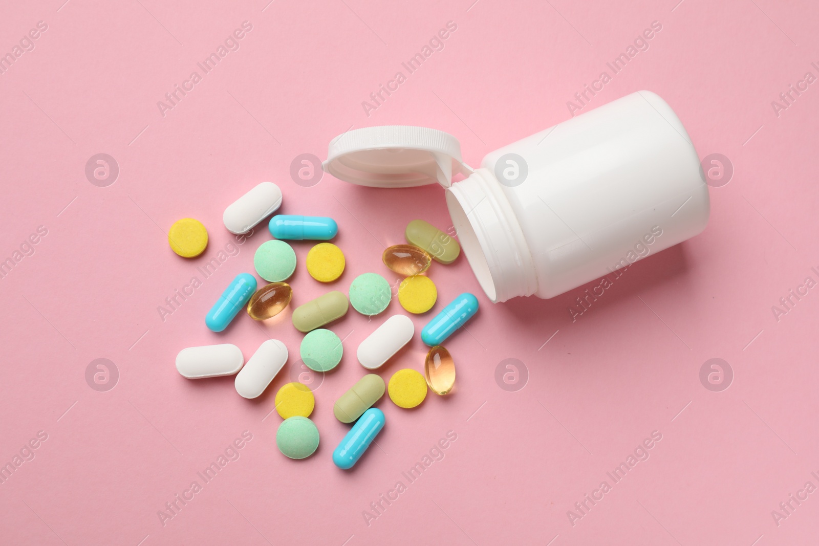 Photo of White bottle and different vitamin pills on pink background, top view