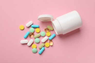 Photo of White bottle and different vitamin pills on pink background, top view