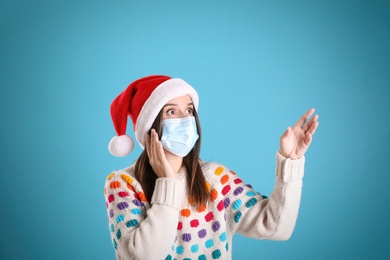 Photo of Surprised woman in Santa hat and medical mask pointing on light blue background