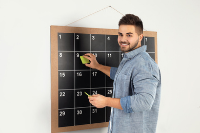 Photo of Young man putting sticky note on board calendar