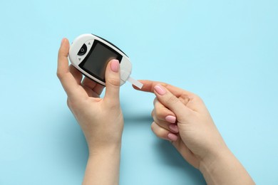 Diabetes. Woman checking blood sugar level with glucometer on light blue background, top view