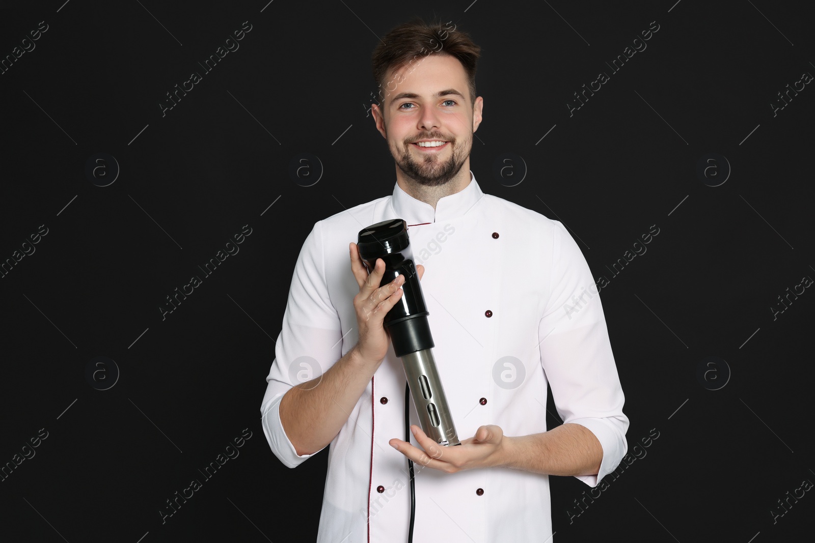 Photo of Smiling chef holding sous vide cooker on black background