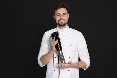 Photo of Smiling chef holding sous vide cooker on black background