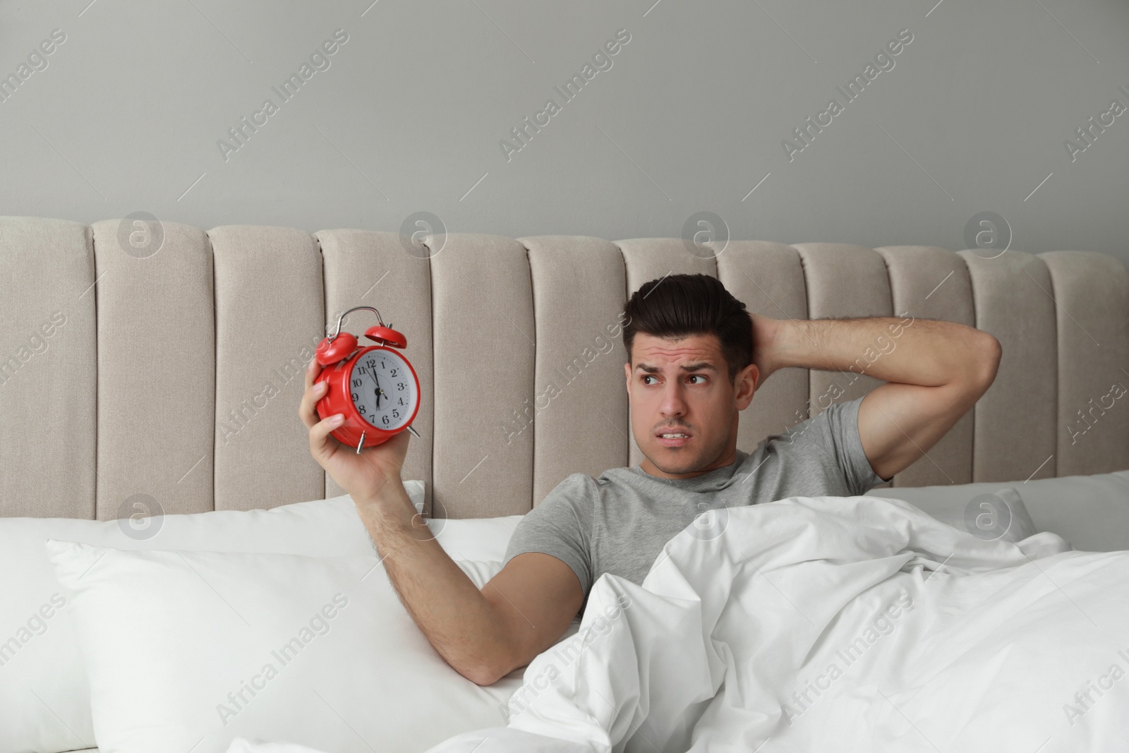 Photo of Emotional man with alarm clock in bed. Being late because of oversleeping