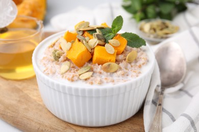 Photo of Tasty wheat porridge with pumpkin and mint in bowl on table, closeup