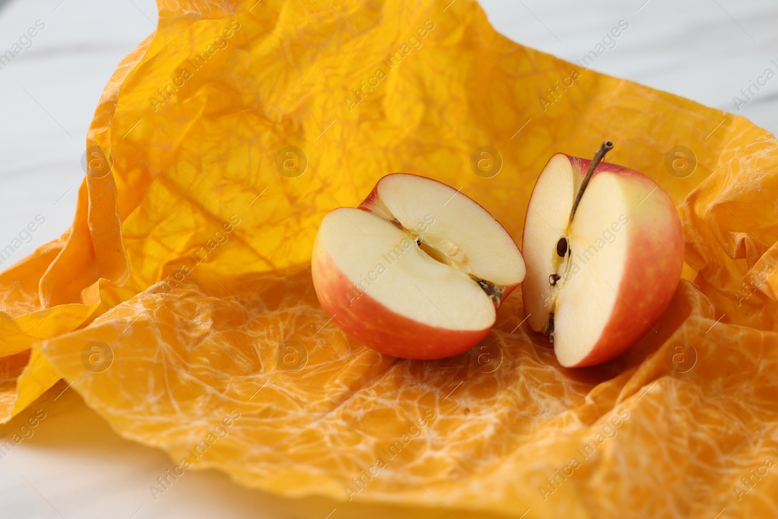 Photo of Halves of apple with orange beeswax food wrap on table, closeup