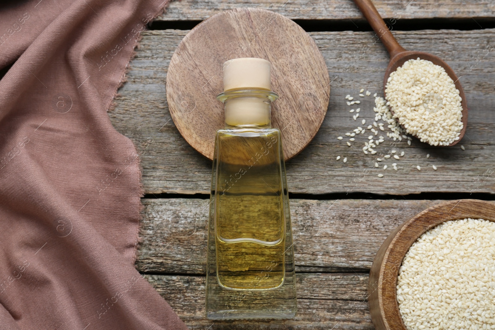 Photo of Bottle of organic sesame oil and seeds on wooden table, flat lay
