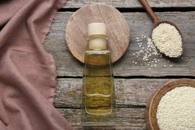 Bottle of organic sesame oil and seeds on wooden table, flat lay