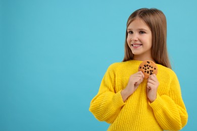 Photo of Cute girl with chocolate chip cookie on light blue background. Space for text