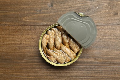 Open tin can of sprats on wooden table, top view
