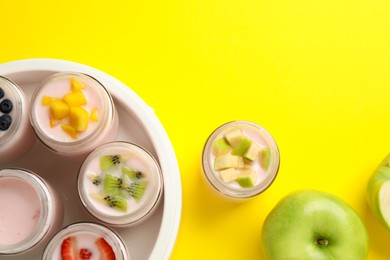 Photo of Tasty yogurt in glass jars and ingredients on yellow background, flat lay. Space for text