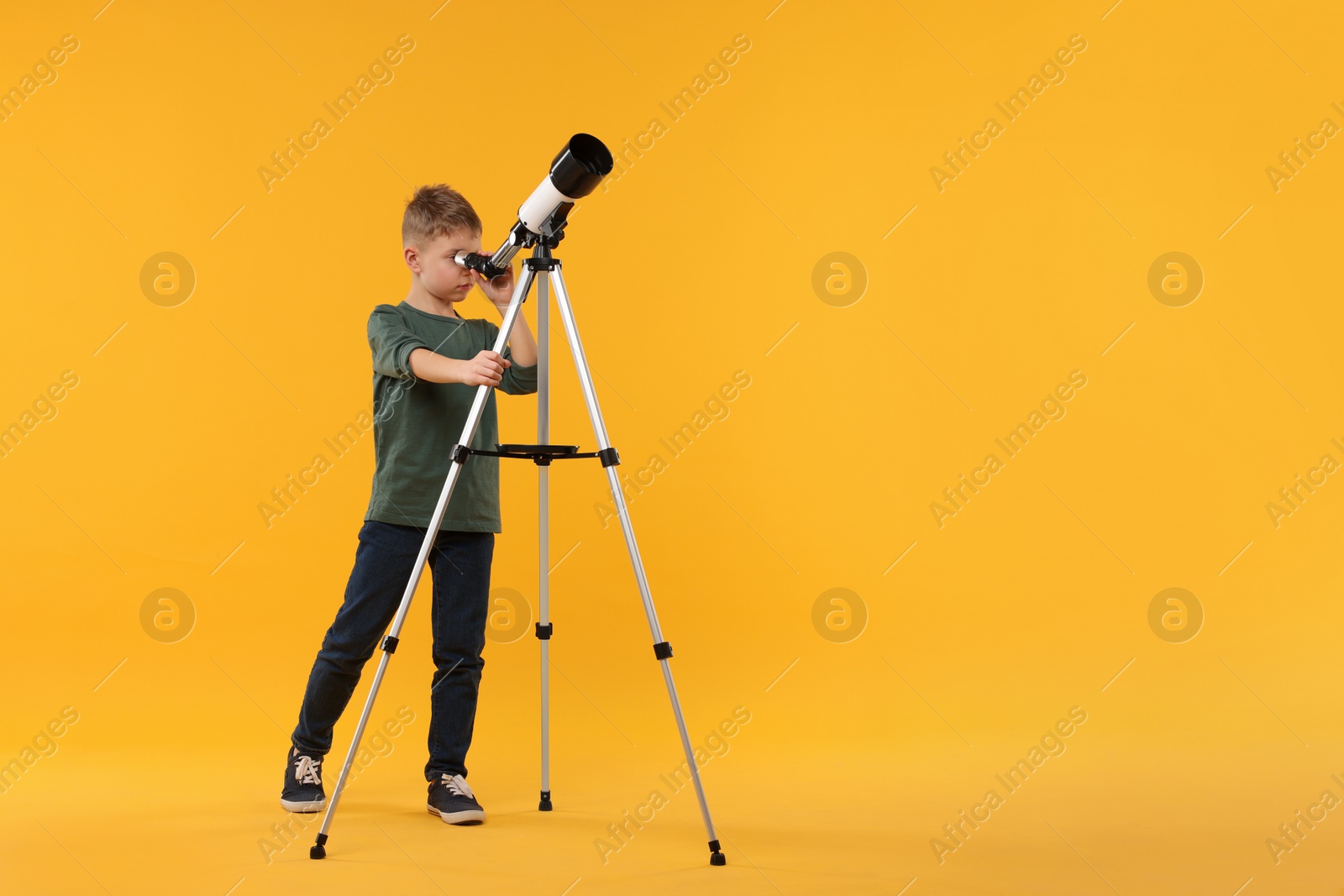 Photo of Little boy looking at stars through telescope on orange background, space for text