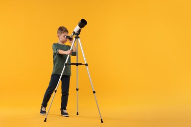 Little boy looking at stars through telescope on orange background, space for text